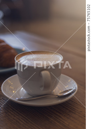 Close up hot cappuccino, latte on table with blur coffee shop background. Hot cappuccino coffee on wood table with blur croissant background. breakfast at coffee shop. softfocus select coffee 75765102