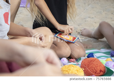 Hand weaving mandalas. A teacher on the beach shows her students how to weave decorative patterns. Creation of special symbols. Training and manual labor concept. Hand weaving mandalas. A teacher on the beach shows her students how to weave decorative patterns. Creation of special symbols. Training and manual labor concept. 75765666