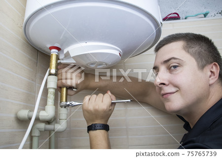 The boiler repair technician uses an adjustable wrench to unscrew or tighten the nut on the pipe. Installing a water heater or dismantling a damaged boiler for later repair. 75765739