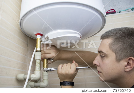 The boiler repair technician uses an adjustable wrench to unscrew or tighten the nut on the pipe. Installing a water heater or dismantling a damaged boiler for later repair. 75765740