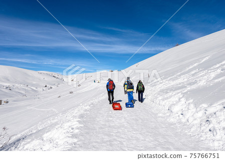Hikers with Rucksacks and Bobsleighs on a Snowy path on Lessinia Plateau - Veneto Italy 75766751