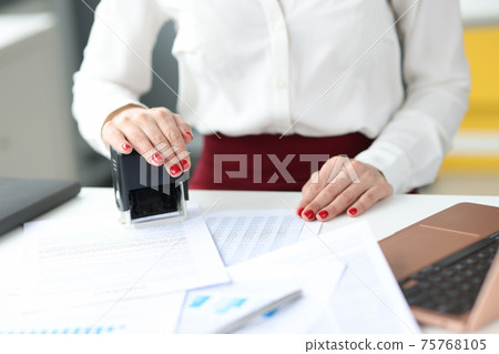 Businesswoman puts stamp on documents on work table 75768105