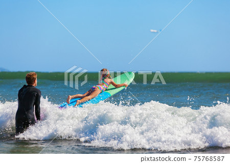Young surfer learn to ride on surfboard with surf instructor Young surfer learn to ride on surfboard with surf instructor 75768587