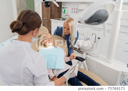 A child with a mother at a dentistry's room. The female child lies in the chair, her mother is behind 75769171