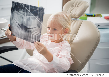 A dentist shows a little girl an x-ray of real teeth 75769640