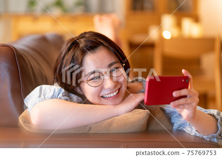 A young woman looking at her smartphone on the sofa in her living room at night 75769753