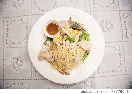 Stir fried rice vermicelli with pork egg and chinese kale, cooked noodles pork vegetable and sauce on white plate on the dining table food 75770026