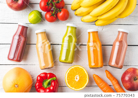 Multicoloured juices in bottles on white wooden background with fruits and vegetables. Top view 75770343
