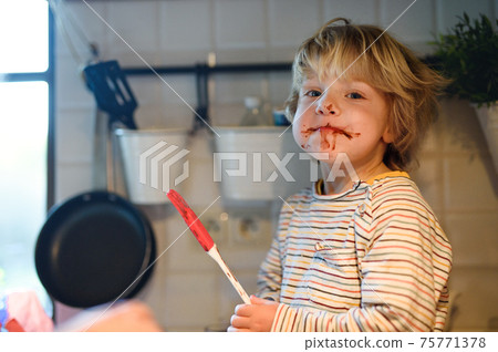 Small boy indoors in kitchen at home, helping with cooking. Small boy indoors in kitchen at home, helping with cooking. 75771378
