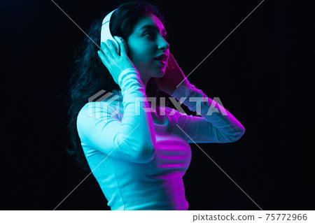 Young beautiful girl in headphones isolated on dark background in neon light 75772966