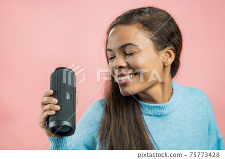 African woman listening to music by wireless portable speaker - modern sound system. Lady dancing 75773428