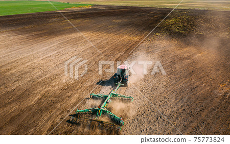 Aerial View. Tractor Plowing Field. Beginning Of Agricultural Spring Season. Cultivator Pulled By A Tractor In Countryside Rural Field Landscape. Dust Rises From Under Plows Aerial View. Tractor Plowing Field. Beginning Of Agricultural Spring Season. Cultivator Pulled By A Tractor In Countryside Rural Field Landscape. Dust Rises From Under Plows 75773824