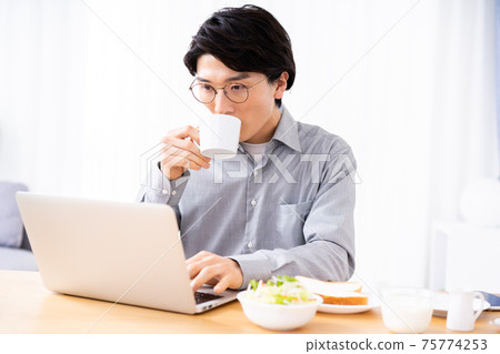 Young man using a laptop while eating breakfast 75774253