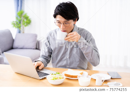 Young man using a laptop while eating breakfast 75774255