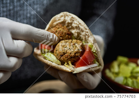 man fills a pita bread with some falafel man fills a pita bread with some falafel 75774703