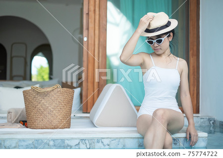 Happy woman in white swimsuit swimming in luxury pool hotel, young female with hat enjoy in tropical resort. Relaxing, summer travel, holiday, vacation and weekend concept Happy woman in white swimsuit swimming in luxury pool hotel, young female with hat enjoy in tropical resort. Relaxing, summer travel, holiday, vacation and weekend concept 75774722