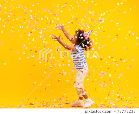 Excited African American kid jumping and catching confetti in studio Excited African American kid jumping and catching confetti in studio 75775235