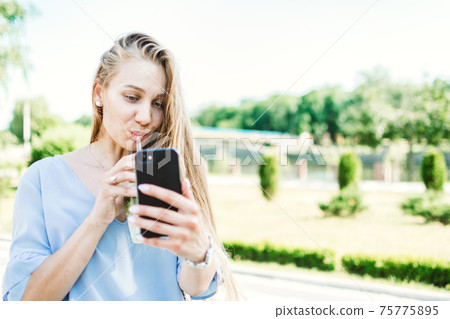 Summer non-alcoholic drink, refreshing cold drink. Young blond woman drinking non-alcoholic mojito in summer city street. 75775895