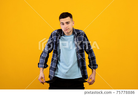 Upset young guy showing empty pockets on orange studio background Upset young guy showing empty pockets on orange studio background 75778886