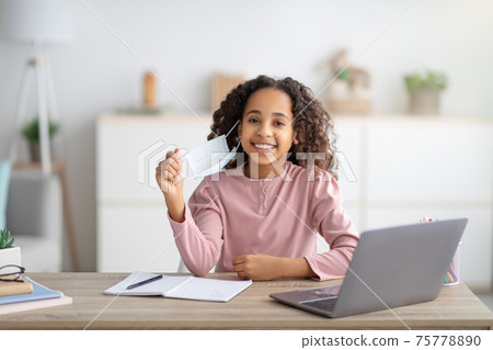 Remote education during lockdown. Black girl wearing medical face mask studying at home on laptop 75778890