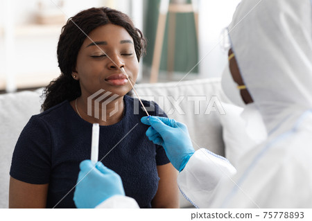 Doctor in protective suit takes swab to patient at home 75778893