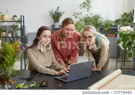 Three Young Women Looking at Laptop Screen in Flower Shop Three Young Women Looking at Laptop Screen in Flower Shop 75779495