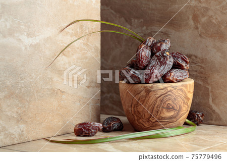 Dates fruit in a wooden bowl on a beige ceramic table. Dates fruit in a wooden bowl on a beige ceramic table. 75779496