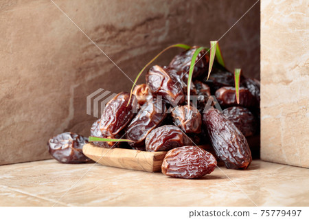 Dates fruit in a wooden dish on a beige ceramic table. 75779497