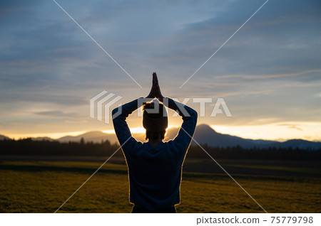 View from behind of a young woman meditating with her hands joined above her head outside 75779798