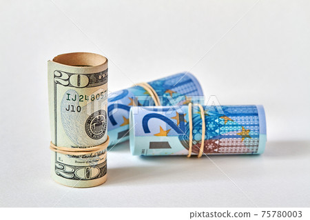 Twenty dollar bill rolled up as a tubule stands on the background of twenty euro bills. Concept of dollar superiority over euro. Closeup, selective focus Twenty dollar bill rolled up as a tubule stands on the background of twenty euro bills. Concept of dollar superiority over euro. Closeup, selective focus 75780003