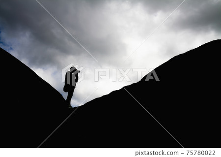 Silhouette of a man in the mountains is taking pictures of the landscape 75780022