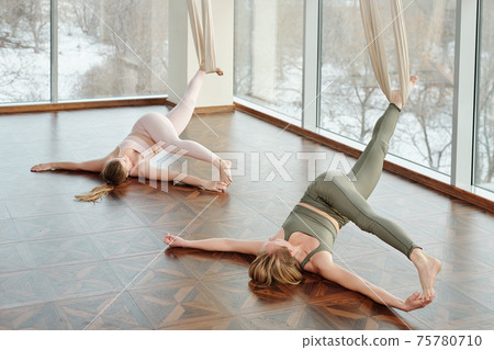 Young active women practicing fly yoga in gym with their legs stretched and hands touching feet Young active women practicing fly yoga in gym with their legs stretched and hands touching feet 75780710