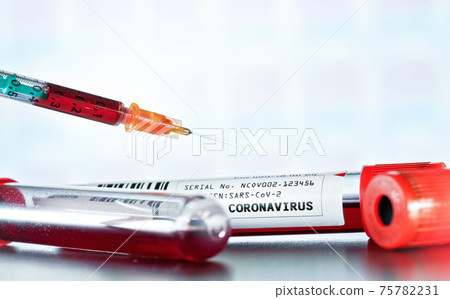 Sample vial with blood, label says coronavirus test (sticker is own design, dummy barcode and data), syringe above, closeup detail. Blurred laboratory equipment background. Covid 19 outbreak concept 75782231
