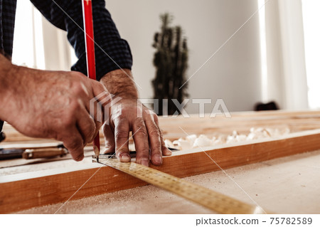Carpenter makes pencil marks on a wood plank 75782589