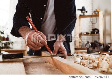 Carpenter makes pencil marks on a wood plank Carpenter makes pencil marks on a wood plank 75782615