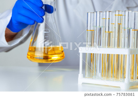 Scientist or doctor in blue gloves pouring some yellow liquid into a flask 75783081