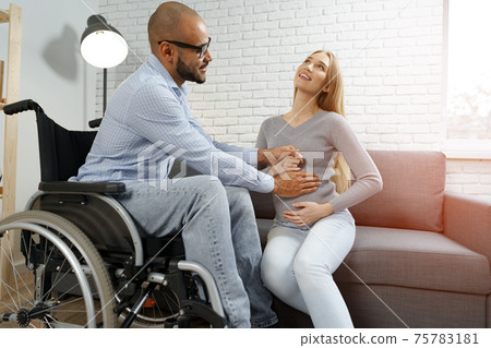 Disabled african american man touching the belly of his pregnant caucasian wife while they relax on sofa at home Disabled african american man touching the belly of his pregnant caucasian wife while they relax on sofa at home 75783181