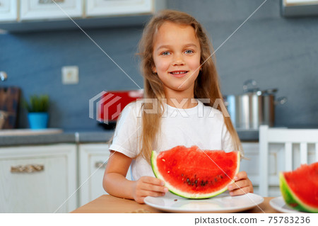 Little girl eating watermelon piece in the kitchen 75783236