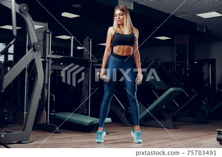 Curvy fit young blonde woman lifting dumbbell in a gym Curvy fit young blonde woman lifting dumbbell in a gym 75783491