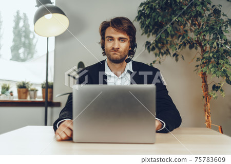 Young man wearing headset doing a video call by laptop 75783609