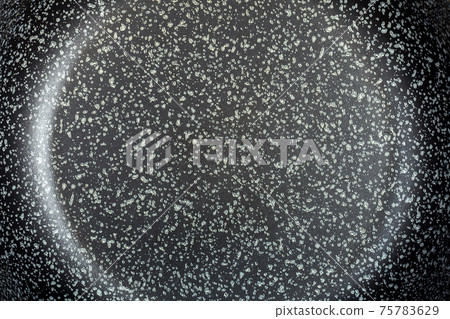 dark surface of a frying pan with a non-stick coating of dark color with dots closeup top view, texture of the coating of kitchen utensils. 75783629