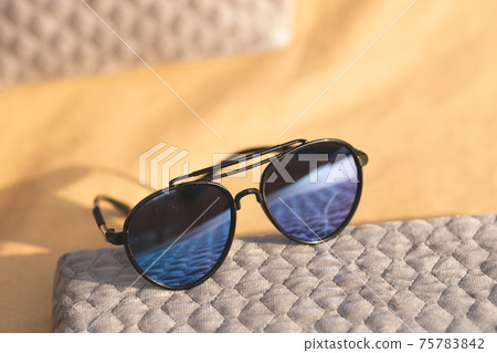 Aviator Sunglasses special model with big blue lenses reflecting the sun in a summer day shoot outdoors closeup . Selective focus Aviator Sunglasses special model with big blue lenses reflecting the sun in a summer day shoot outdoors closeup . Selective focus 75783842