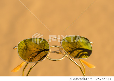 Classic sunglasses model with golden lenses shoot outside in a sunny day closeup . Selective focus Classic sunglasses model with golden lenses shoot outside in a sunny day closeup . Selective focus 75783844