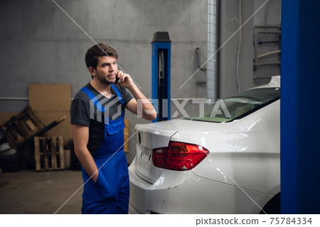 A man is standing by the car and talking on the phone A man is standing by the car and talking on the phone 75784334