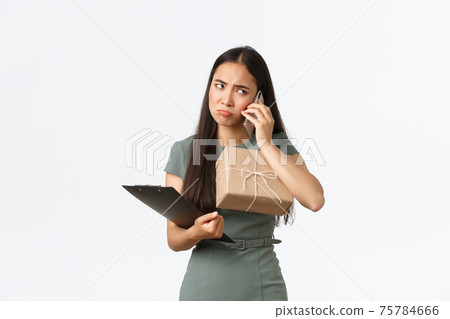 Upset pouting asian businesswoman holding clients package and clipboard with customer info, manage small business from home, talking with angry client, feeling sad about negative feedback Upset pouting asian businesswoman holding clients package and clipboard with customer info, manage small business from home, talking with angry client, feeling sad about negative feedback 75784666