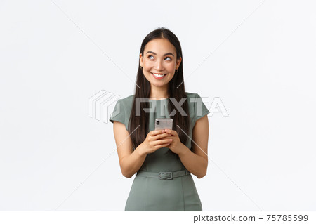 Small business owners, women entrepreneurs concept. Dreamy smiling stylish asian blogger, looking upper left corner thoughtful, creating content, thinking while texting message, using smartphone 75785599