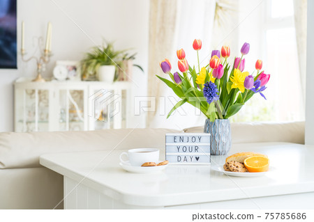 Good morning concept. Romantic breakfast - fresh spring flowers, cup of hot coffee drink, cookies, orange, lightbox with message Enjoy your day on marble table with light interior view. Copy space. Good morning concept. Romantic breakfast - fresh spring flowers, cup of hot coffee drink, cookies, orange, lightbox with message Enjoy your day on marble table with light interior view. Copy space. 75785686