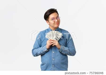 Smiling smart asian male entrepreneur, freelancer in glasses holding money and looking satisfied, earn cash for working on project, made good investment, standing white background 75786046