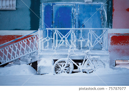 Bicycle near the entrance of the building, covered with frost and snow 75787077