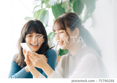 看智能手機的兩名微笑的婦女在咖啡館 75790288